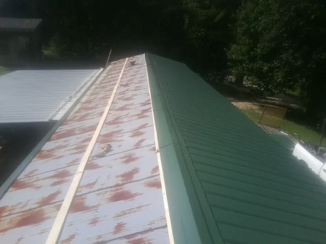 Old rusted panels beside newly installed green metal roofing — Wind Damage Roof Repair by Roofing Brothers in Warren